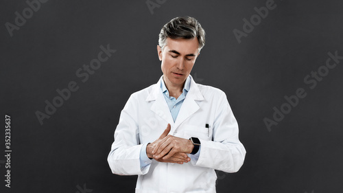 Stay safe. Mature male doctor in medical uniform showing how to wash hands while standing against black background