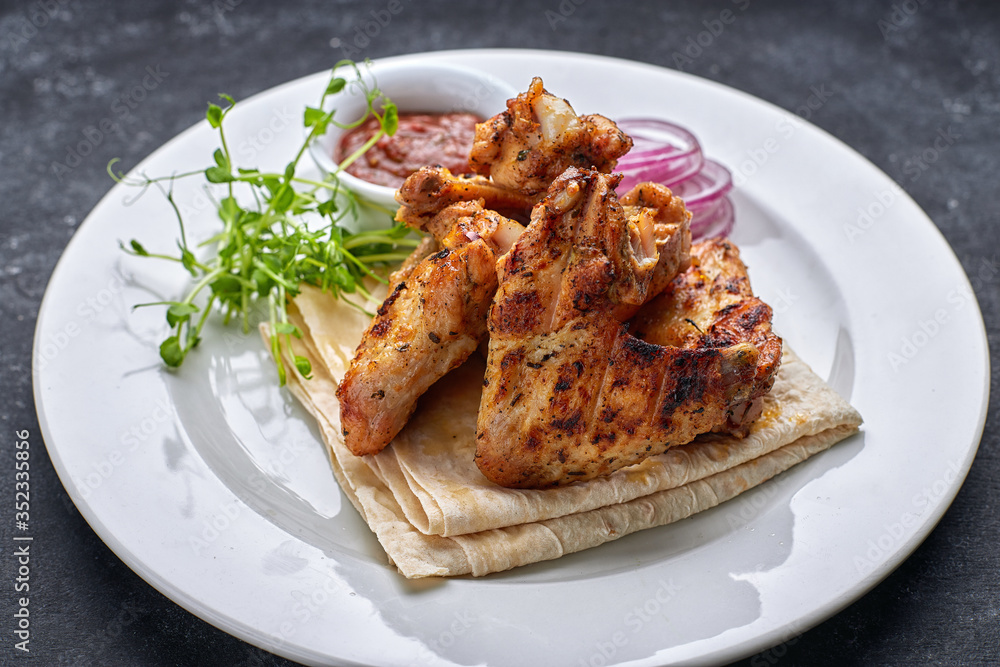Grilled chicken wings with barbecue sauce, pita bread, microgreen and onion rings, on a white plate, against a dark background Grilled chicken wings with barbecue sauce, pita bread, microgreen and onion rings, on a white plate, against a dark background