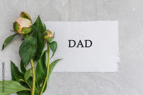 Gray paper background with peony flowers and a card with the inscription dad. © Elena Shi