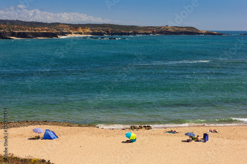 People bathing at the beach in Vila Nova de Milfontes  on hot summer day  blue sky  crystalline water