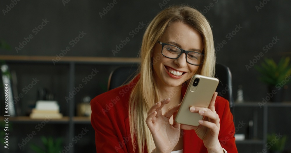 Close up of smartphone in hands of blonde businesswoman. Happy female texting message and typing on cellphone in cabinet.