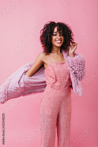 Bold, charming girl with cute curls is charged with positive and pleases eye with snow-white smile