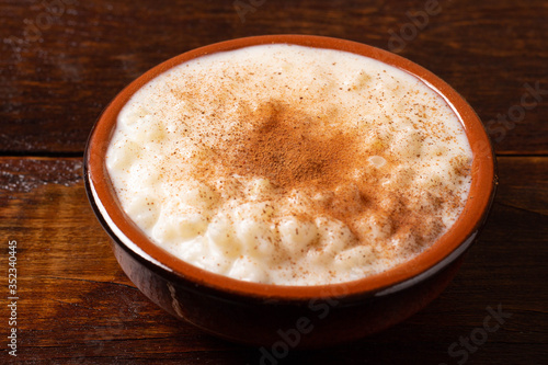 White corn cooked with milk known as canjica, canjicão or mungunza, in a rustic bowl on wooden table. Typical dish of Brazilian Party called Festa Junina.
