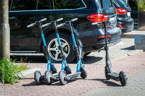 Row of electric kick scooters standing on the street against modern car.