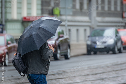 a man walks under an umbrella along the road and tram tracks.