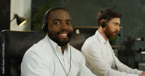 Portrait of handsome African American young man in headset working at computer in call center.