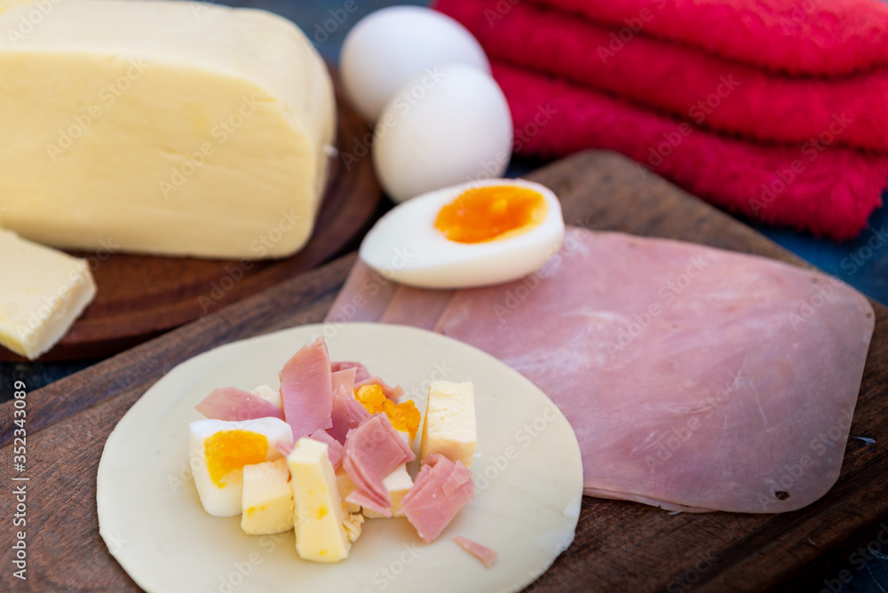 Empanada de jamón y quesos, sus ingredientes, primer plano sobre una tabla de madera rústica Empanada de jamón y quesos, sus ingredientes, primer plano sobre una tabla de madera rústica