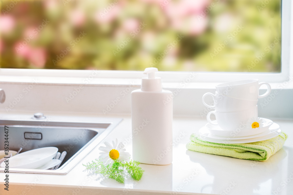 Eco friendly non-toxic cleaning dish soap with natural ingredients, chamomile flowers, clean white cups and plates near sink with dirty dish. Skincare for housekeeping. Bio organic cleaning supplies.