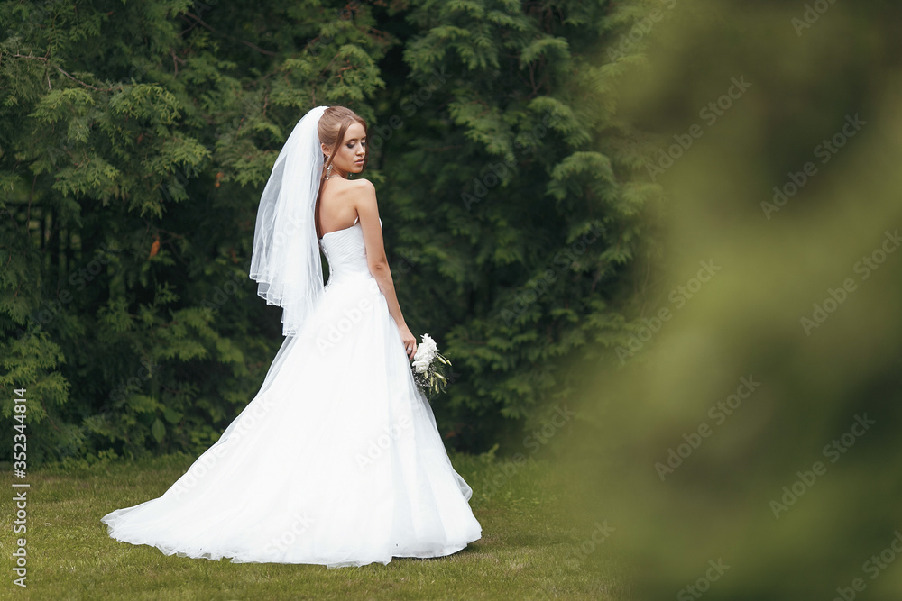 Beautiful bride in a magnificent wedding dress posing among greenery on the street. Dvushka poses in a wedding dress for advertising. Bride concept for advertising dresses