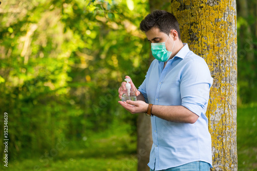 Man with protective face mask standing in the park, using wash hand alcohol gel, against coronavirus disease Covid-19 . Antiseptic, Hygiene and Health concept . photo