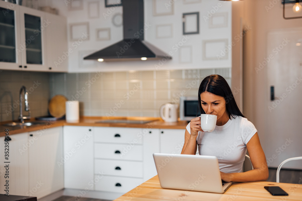 Beautiful woman at kitchen table, drinking tea and using laptop, portrait. Beautiful woman at kitchen table, drinking tea and using laptop, portrait.