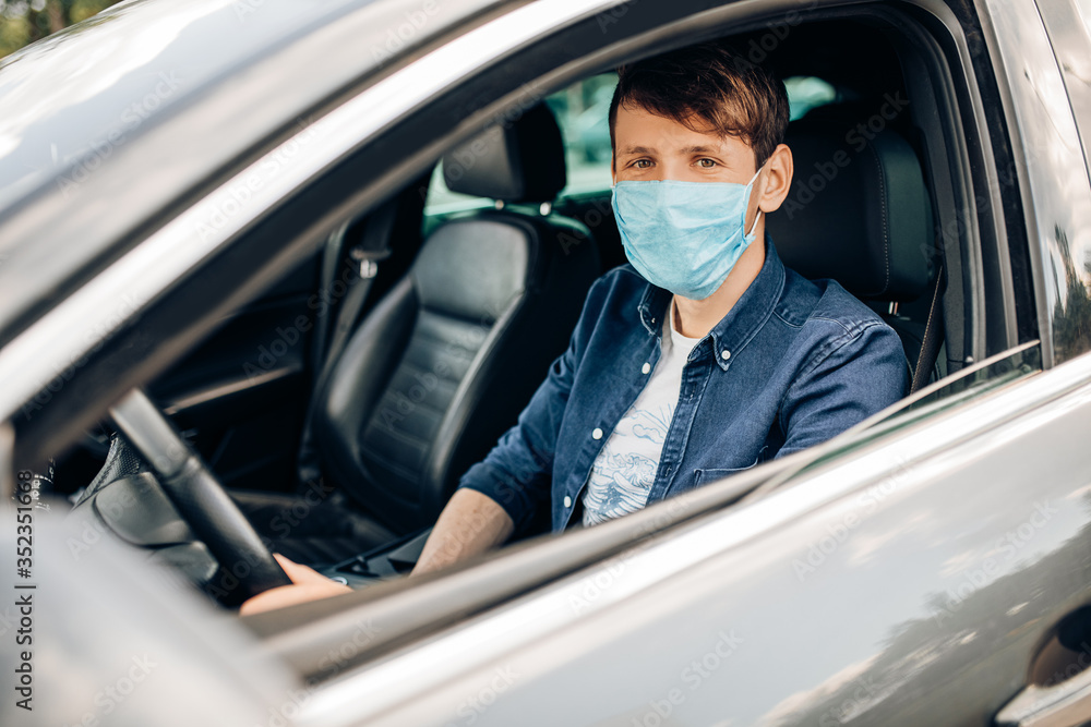 A man in a protective medical mask, sitting behind the wheel of a car. Quarantine, coronavirus A man in a protective medical mask, sitting behind the wheel of a car. Quarantine, coronavirus