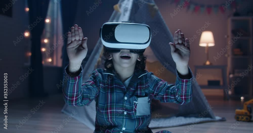 Funny little kid wearing pajamas is putting on virtual reality headset