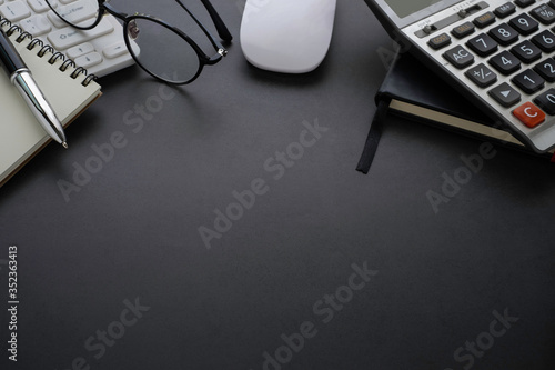 Workplace office with dark grey desk. Close-up view from above of keyboard, glasses with notebook and mouse. Tabletop space for creative work. Flat lay with copy space. Business and finance concept.