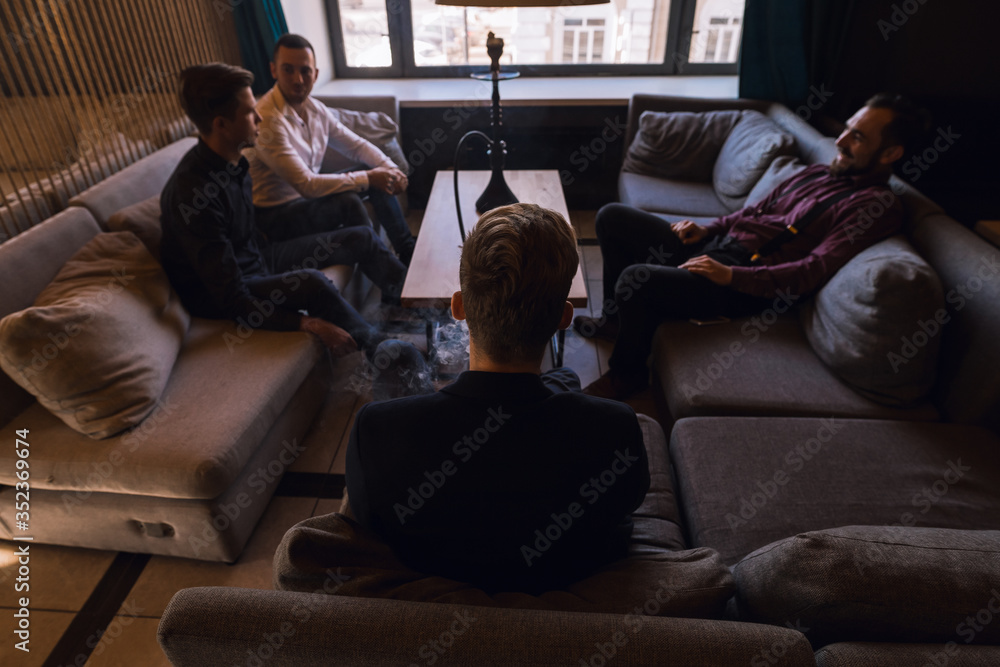 Men relax and smoke hookah in a stylish loft cafe with a modern design. Men relax and smoke hookah in a stylish loft cafe with a modern design.