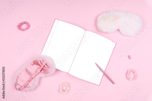 Journal with cute fluffy sleep masks and pink accessories. Sleep management and optimization, beauty sleep and sleep log concept. Place for text