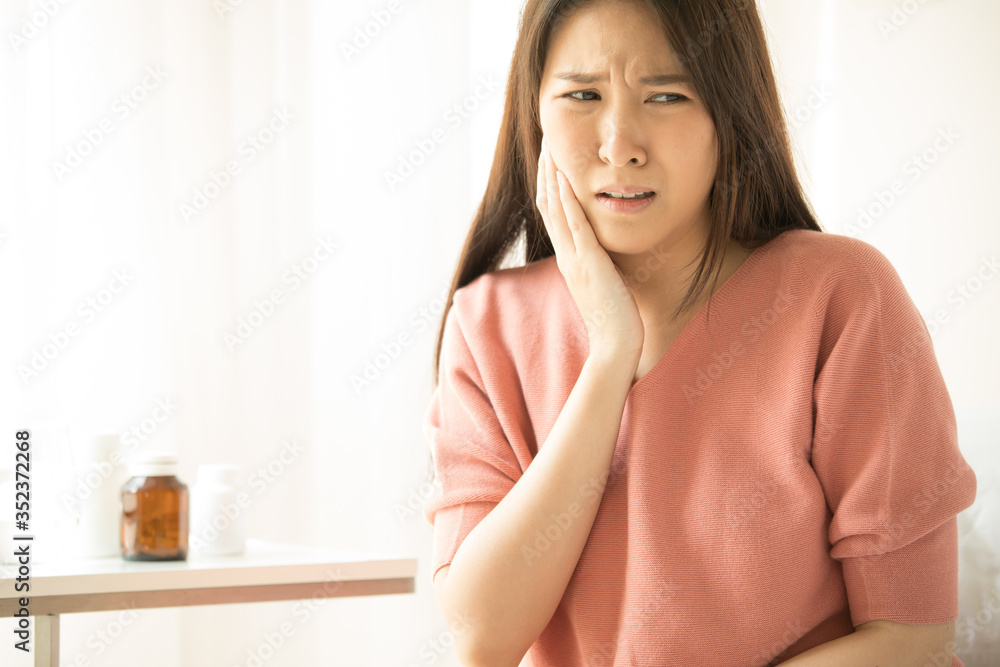 Woman is sitting on bed in her home, she has toothache. concepts of health and medical care Woman is sitting on bed in her home, she has toothache. concepts of health and medical care