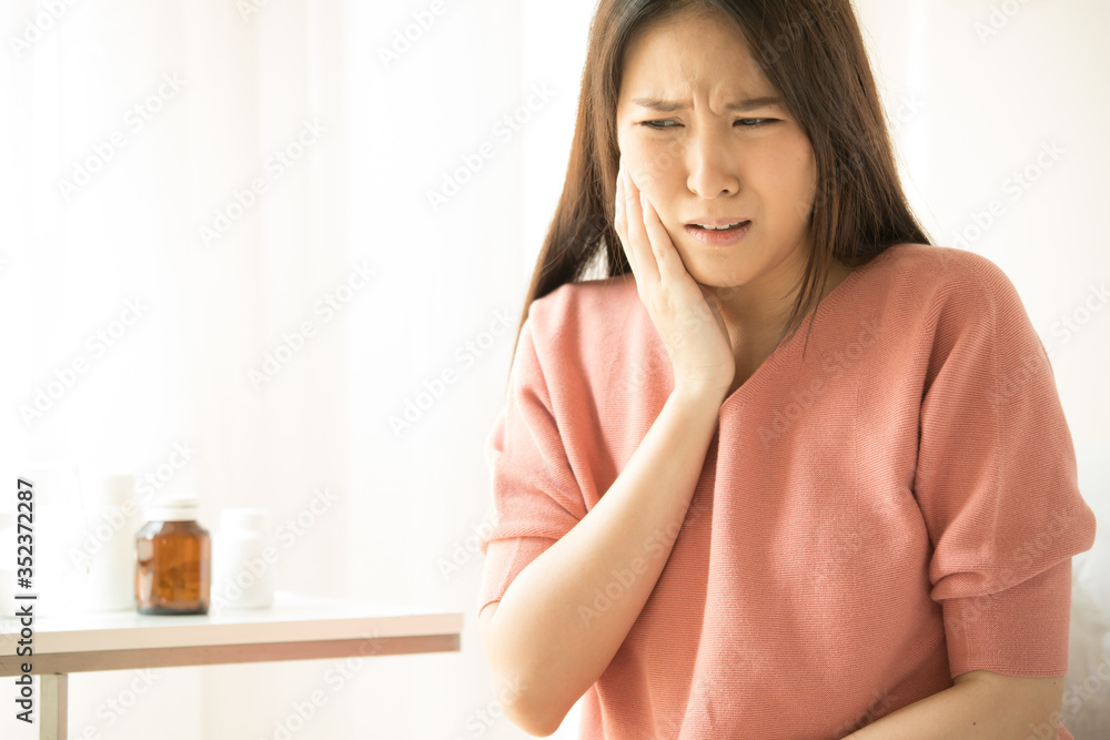 Woman is sitting on bed in her home, she has toothache. concepts of health and medical care Woman is sitting on bed in her home, she has toothache. concepts of health and medical care