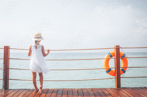 Suntanned girl in white dress enjoyes sea view at the wooden pier. Vacation, get away, travel concept. Toned image, place for text