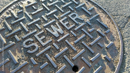 Extreme closeup of metal sewer cap on a dry, cracking road during summer