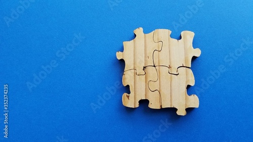 Wood surface puzzle pieces close up view on clean blue background, concept of teamwork