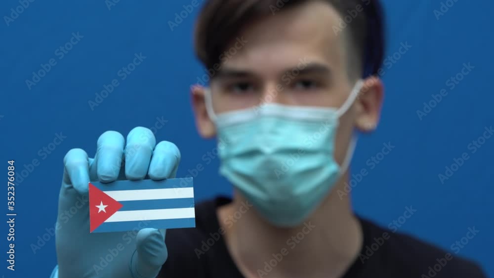 COVID-19 pandemic in Puerto Rico. A young, attractive Puerto Rican man, Latin American, wearing a protective medical mask and gloves. The guy is holding the flag of Puerto Rico. Coronavirus disease COVID-19 pandemic in Puerto Rico. A young, attractive Puerto Rican man, Latin American, wearing a protective medical mask and gloves. The guy is holding the flag of Puerto Rico. Coronavirus disease