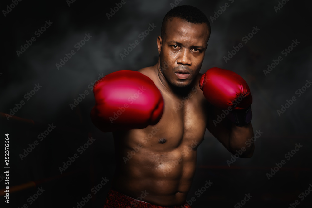 african american boxer punching with glove in dark background