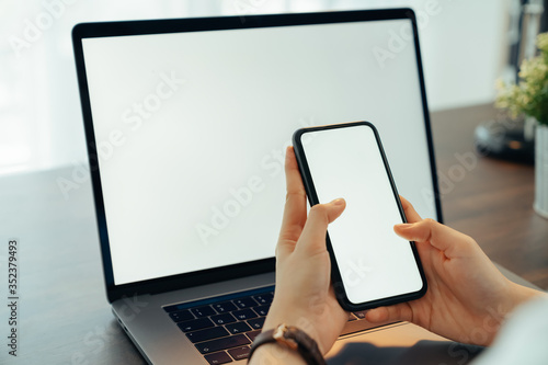 Woman hand holding smartphone with blank copy space screen for your advertisement. laptop on the table.