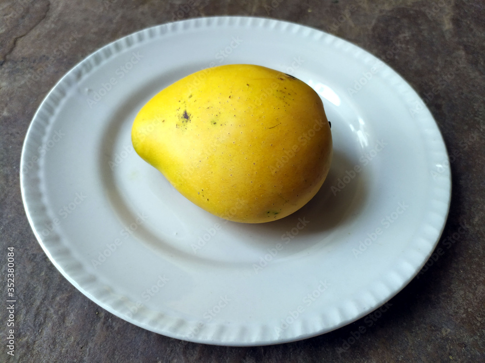 fresh sweet yellow mango put in a white plate  isolated on stone background