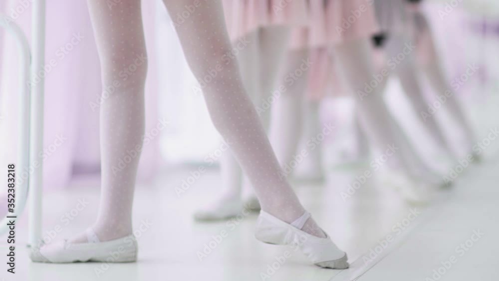 Close up feet of unrecognizable little girls in white socks and ballet shoes, their ballet teacher correcting them Close up feet of unrecognizable little girls in white socks and ballet shoes, their ballet teacher correcting them