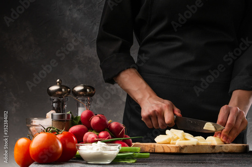 The chef cuts potatoes for cooking potatoes in French. Against the background of vegetables. With space for advertising, restaurant business, and cooking. Book of recipes