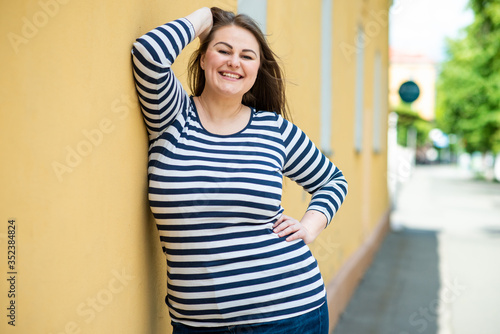 Smiling cheerful woman plus size posing outdoors on orange wall background