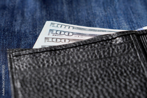 Black genuine leather wallet with banknotes inside, jeans background. Soft focus