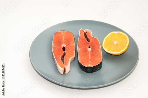 Close up fresh raw salmon red fish steak with lemon slice on a plate, isolated on white background