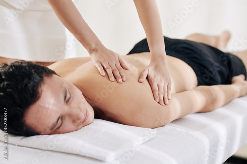 Masseuse making gliding movements in long even strokes when spreading warmed oil across the back of person
