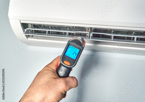 Engineer checking temperature by infrared thermometer inside of air conditioner.
