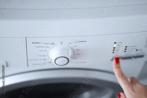 The girl sets the washing program for the washing machine.