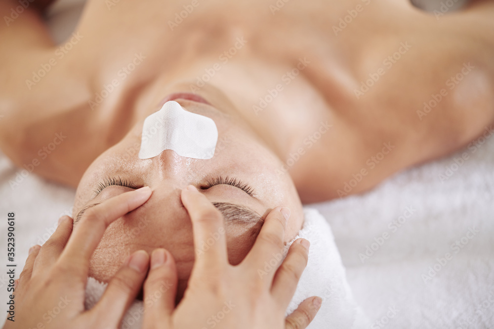 Fototapeta premium Man with nose strip getting anti-aging and refreshing face massage in beauty salon