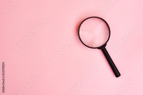 Close up Single Magnifying Glass with Black Handle, Leaning on pink background.