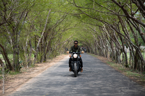 Tourists ride a classic motorbike on a sunny day on the tree tunnel road. Motorcycle riding concept