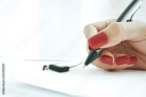 Close up of a woman hand holding a black pen and writing on a blank paper.
