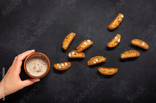 Cup of cappuccino in hand and Biscotti biscuits on a black background. Top view. 