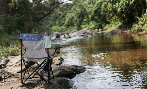 There are chairs arranged by the stream with clear water and fresh natural forest. With a face mask hanging on the chair.Concept of defeating illness.Recovered from coronavirus.Cured disease emotional