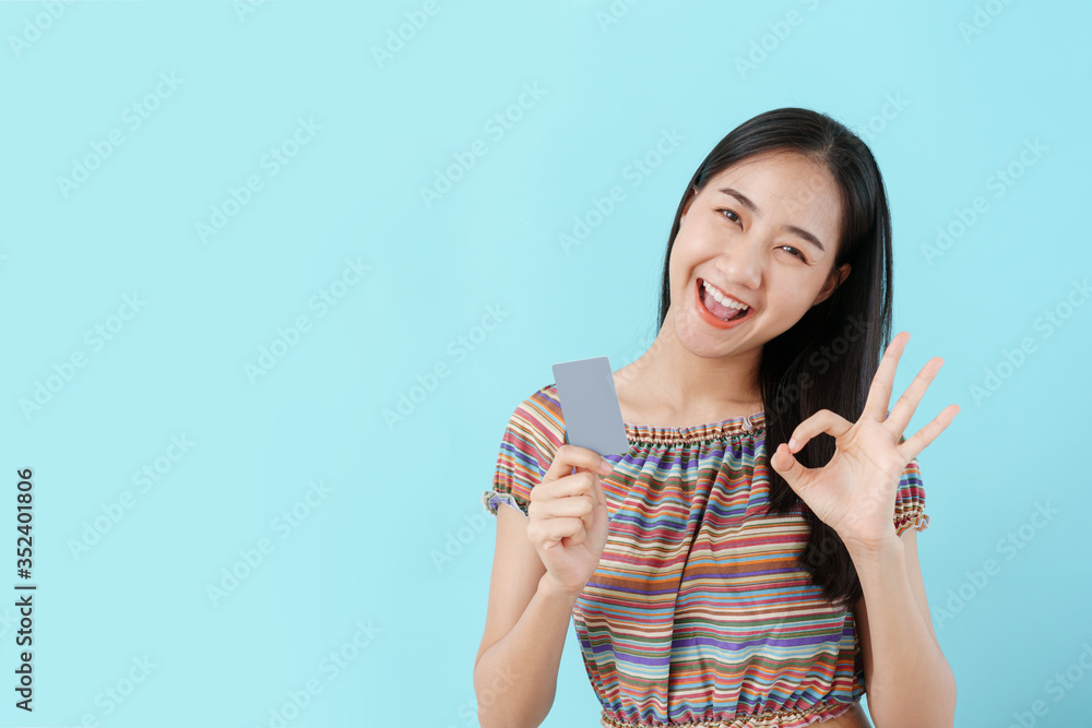 Beautiful young Asian girl holding blank credit card and ok hand women on background blue isolated. Asia women happy smile and copy space Beautiful young Asian girl holding blank credit card and ok hand women on background blue isolated. Asia women happy smile and copy space