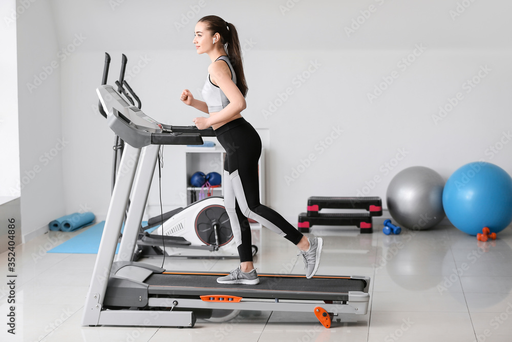 Fototapeta premium Sporty young woman training on treadmill in gym