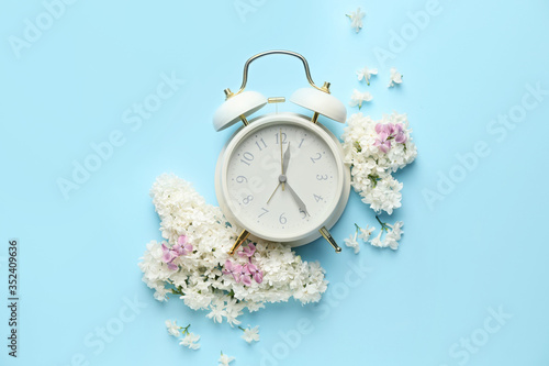 Composition with beautiful lilac flowers and alarm clock on color background