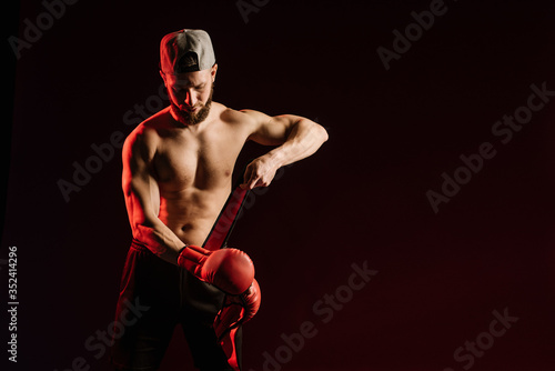 Young muscular man looking aggressive with boxing gloves on black background © rostyslav84