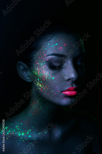 Fashion model woman in neon light bright fluorescent makeup  drop on face. Beautiful model brunette girl colorful make-up  painted skin  body art design ultraviolet
