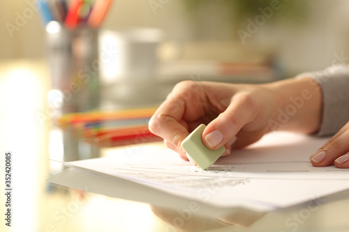 Woman erasing drawing with rubber on desk at home
