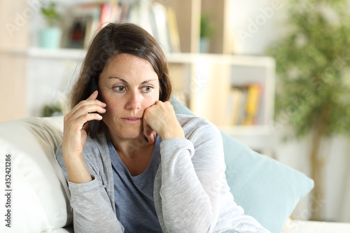 Pensive middle age woman calling on phone at home